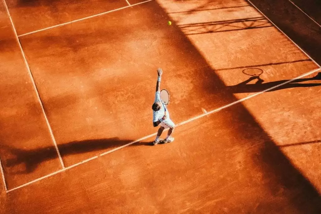 Man ready to serve during a tennis match on an orange court
