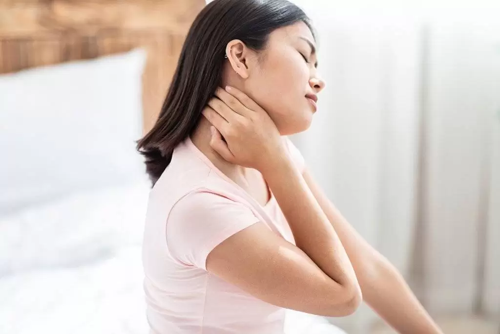 Asian Woman Having Arthritis Massaging Aching Neck Sitting In Bed At Home.